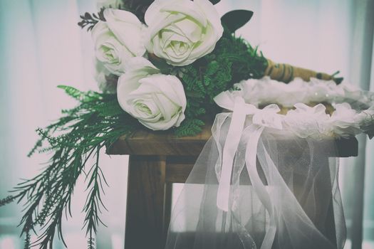 wedding white bridal veil & rose flower bouquet on wooden chair beside see through sheer window curtain