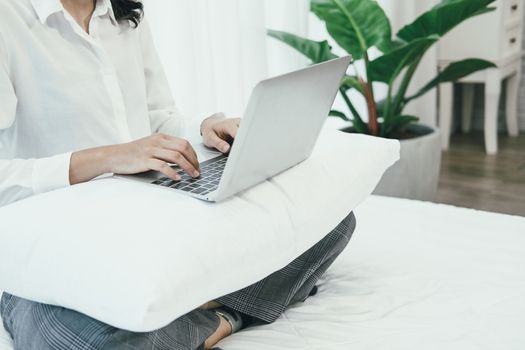 asian woman using computer laptop on bed in bedroom. work remotely  at home. leisure lifestyle