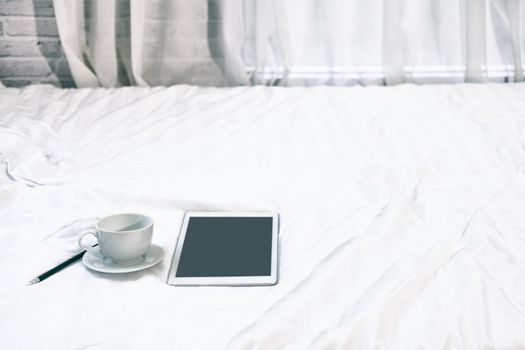 tablet coffee cup pencil on white bed in bedroom