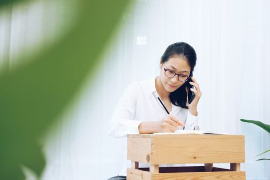 freelancer woman businesswoman talking on mobile phone writing note on bed at home