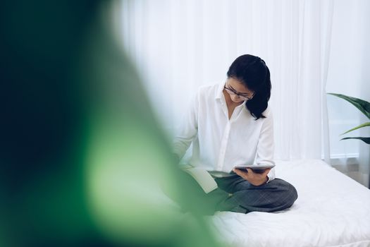 asian woman writing note watching video on tablet. student listen lecture study online course on bed in bedroom at home