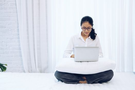 asian woman using computer laptop on bed in bedroom. work remotely  at home. leisure lifestyle