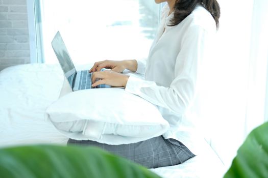 asian woman using computer laptop on bed in bedroom. work remotely  at home. leisure lifestyle
