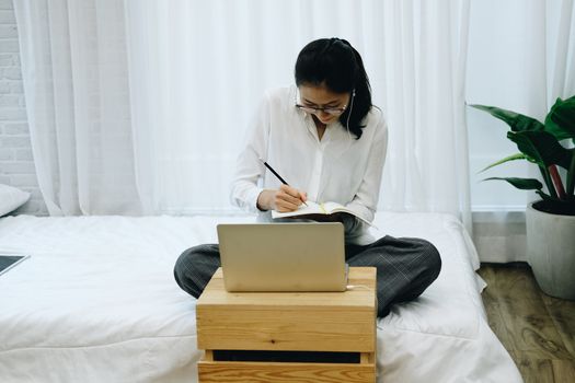asian woman wearing earphones writing note watching video. student listen lecture study online course