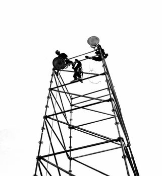 Workers set up powerful lights on scaffolds, seen in silhouette
