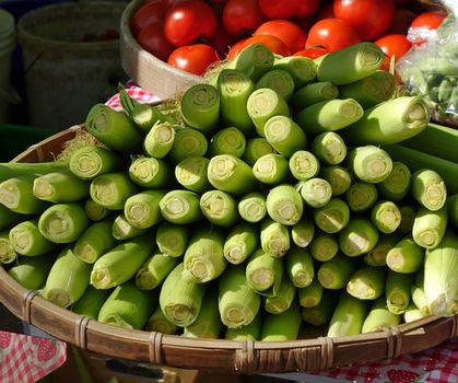 A market stall sells fresh baby corn and ripe red tomatoes
