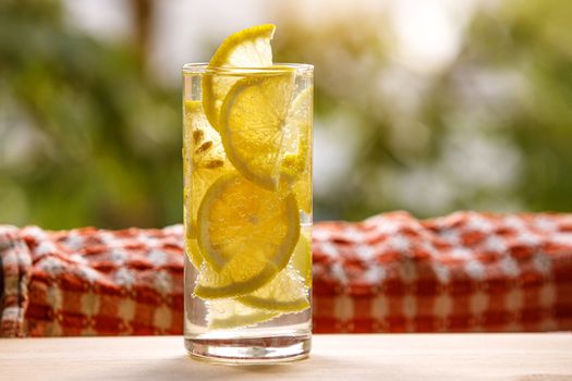 Glass of lemonade with lemon on sunny garden background