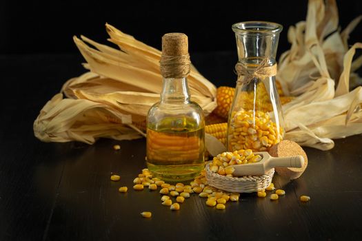 Corn oil and corn kernels on black blackground.