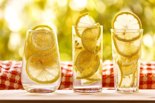 Glasses of lemonade with lemon on the sunny garden background