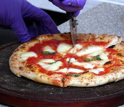 Pizza margherita with tomatoes, cheese and fresh basil is being cut before serving