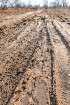 Deep tires tracks on the road covered by wet muddy sand