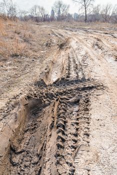 Deep tires tracks on the road covered by wet muddy sand
