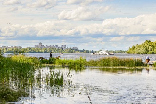 KIEV/UKRAINE - JUNE 18, 2014 - Fishers and a white boat on the Dnieper River in Kiev, Ukraine. A view of the city in the distance, under a spring cloudy sky.