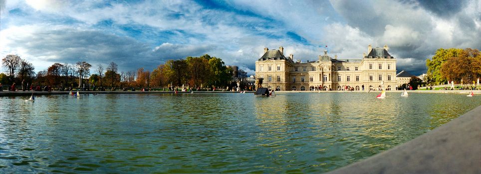 panoramic view of the fountain of jardin de Luxembourg in warm autumnal light and a blue sky with some wooden little boats on it