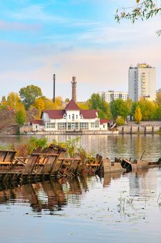 Wrecked boat on the Dnieper river in Kiev, Ukraine, in autumn. In the background, ypou can see an uninhabited floating house. Light clouds float in a pale blue sky
