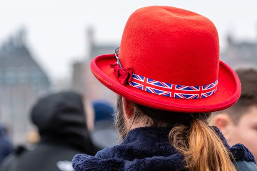 London, UK - January 1, 2020: A man in a red hat with a British flag ribbon in a hat on a defocused London street background. Rear view