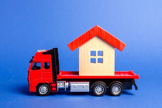 Red truck transports a red roofed house. Concept of transportation and cargo shipping, moving company. Construction of new houses and objects. Industry. Logistics and supply. Move entire buildings.