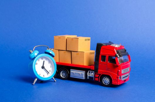 A red truck with cardboard boxes and a blue alarm clock. Express delivery in short time concept. Temporary storage, limited offer and discount. Optimization of delivery logistics. Transport company