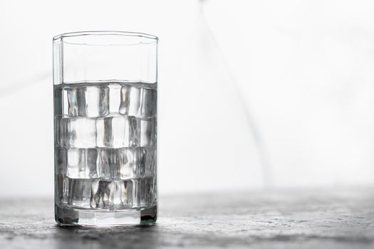Glass of water with ice and light blurred background.