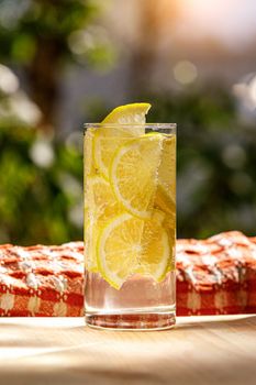 Glass of lemonade with lemon on sunny garden background