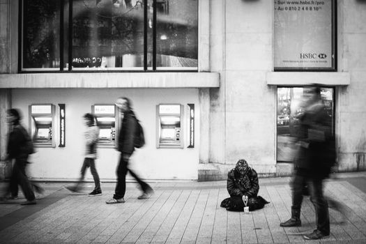 A homeless person begging on the street while people walk by