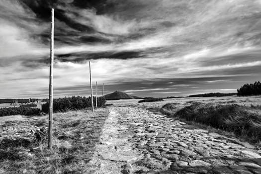 Cobbled road and poles on the tourist trail to Sniezka in autumn in the Giant Mountains in Poland, black and white