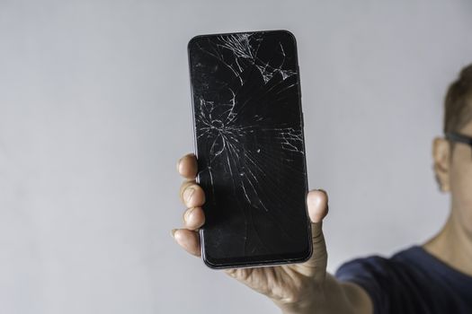 Woman holding a broken touch screen of smart phone on grey background.