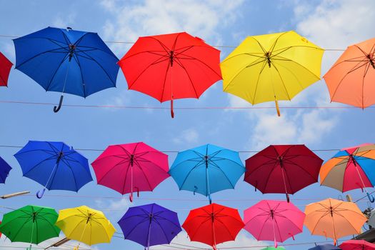 Colorful umbrellas background. Coloruful umbrellas urban street decoration. Hanging Multicoloured umbrellas over blue sky.