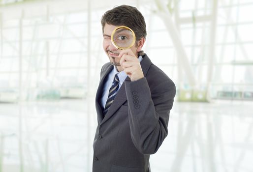 Isolated young business man with magnifying glass, at the office