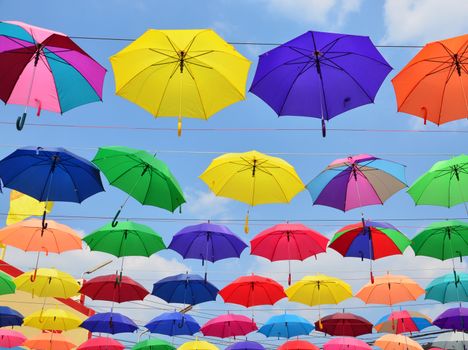 Colorful umbrellas background. Coloruful umbrellas urban street decoration. Hanging Multicoloured umbrellas over blue sky.