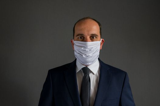 portrait of a smart dressed business man with suit and tie wearing a protective face mask looks into the camera. Gray Background with lots of copy space