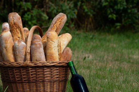 fresh bread in a basket with a bottle of red wine on a meadow