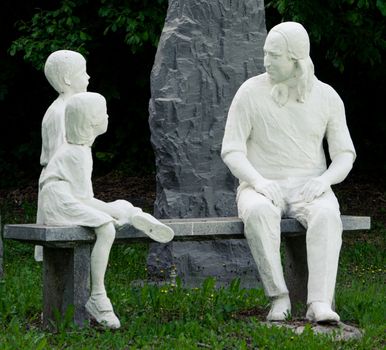 Statue of Nikolaus Ludwig, Reichsgraf von Zinzendorf und Pottendorf teaching children while sitting on a stone bench in a park.