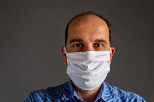 portrait of a young caucasian man wearing a protective face mask in front of a gray background. Studio shot with natural light.