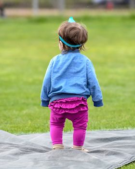 Adorable infant playing with a baseball bat and ball at the baseball park. Cute baby with headband trying to pick up the baseball and also trying to hit the ball with a bat that is too big for her.