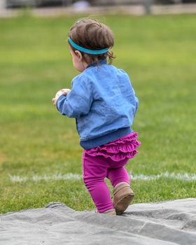 Adorable infant playing with a baseball bat and ball at the baseball park. Cute baby with headband trying to pick up the baseball and also trying to hit the ball with a bat that is too big for her.