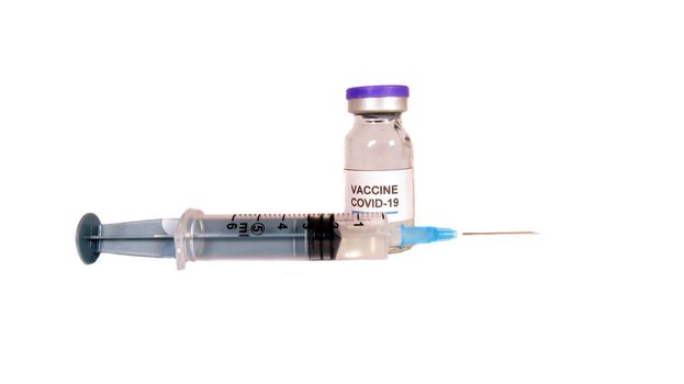 A Covid 19 vaccine bottle and an injection syringe, on white studio background.                               