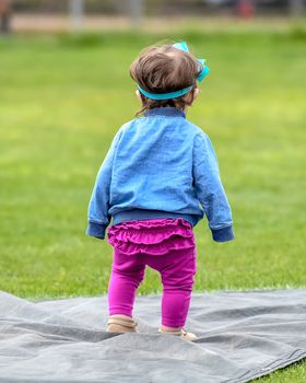 Adorable infant playing with a baseball bat and ball at the baseball park. Cute baby with headband trying to pick up the baseball and also trying to hit the ball with a bat that is too big for her.