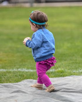 Adorable infant playing with a baseball bat and ball at the baseball park. Cute baby with headband trying to pick up the baseball and also trying to hit the ball with a bat that is too big for her.