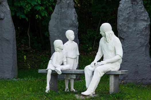 Statue of Nikolaus Ludwig, Reichsgraf von Zinzendorf und Pottendorf teaching children while sitting on a stone bench in a park.