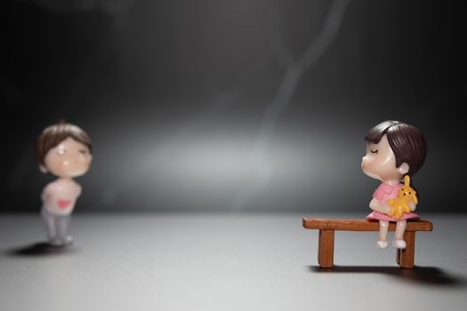 A small cartoon woman sitting on a wooden table showing love, but demonstrating the idea of ​​a distant society to avoid the spread of the corona virus or other contagious diseases.