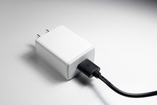White charger adapter and black USB cable on a white background The concept of charging technology to power mobile phones