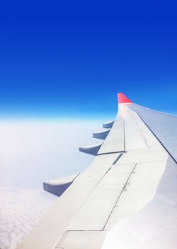 View of a commercial aeroplane from window where you can see the wing which flies above the clouds at height 35,000 feet.
