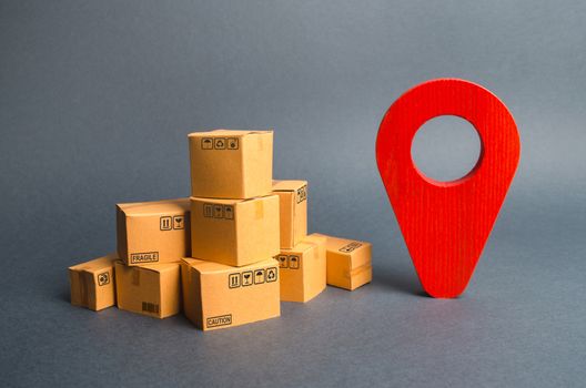 A pile of cardboard boxes and a red position pin. Locating packages and goods. Algorithm for constructing a minimum route for the delivery of orders. Tracking parcels via the Internet.