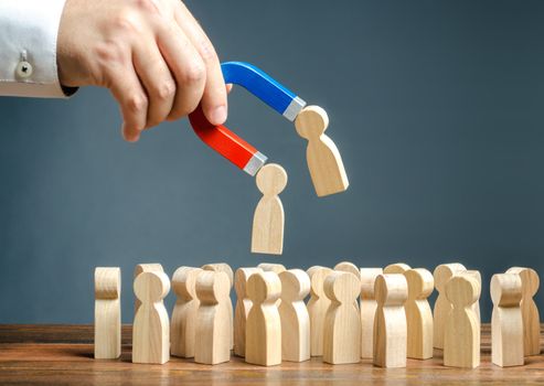 Businessman with a magnet pulling wooden figures of people from the crowd. Recruiting new workers, headhunters. Formation of a new business team of applicants. Personnel Management. Find the best.