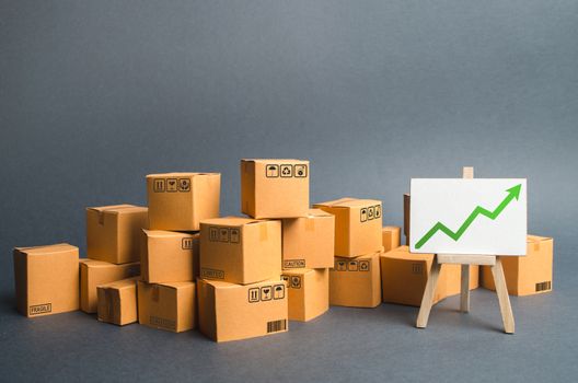 Lots of cardboard boxes and a stand with a green up arrow. rate growth of production of goods and products, increasing economic indicators. Increasing consumer demand, increasing exports or imports.