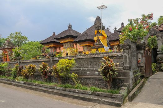 Hindu temple in Bali, Indonesia. Ornamental wall around the temple of black stone. Traditional temple architecture and black fiber coconut palm roofs. Pura Temple in Bali Island, Indonesia