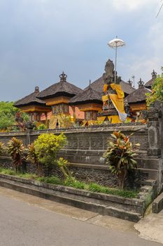 Hindu temple in Bali, Indonesia. Ornamental wall around the temple of black stone. Traditional temple architecture and black fiber coconut palm roofs. Pura Temple in Bali Island, Indonesia