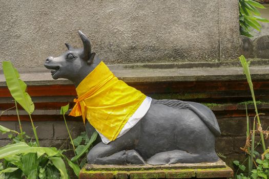 Large carved stone cow guardian statue at Hindu temple in Bali Indonesia. A close up on a guardian figure of wrapped in checked material tied with yellow ribbon. Sculpture of Balinese temple guardian.