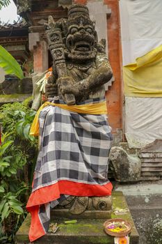 A bricked entrance gate to a Hindu temple on Bali, Indonesia. Entrance gate is closed. There is guardian figure next to it, wrapped in checked material tied with yellow ribbon. A close up.